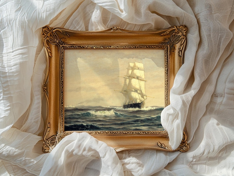 A framed painting of a tall sailing ship on the open sea, with billowing sails and waves crashing against the hull, set against a cloudy sky. The ornate, gold-colored frame surrounds the painting, which is draped with soft, white, flowing fabric.