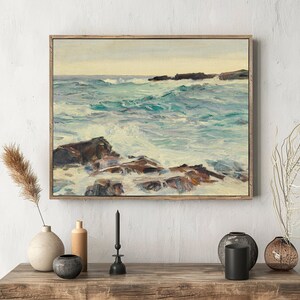 Framed seascape painting on a textured wall shows turbulent waves crashing over rocks. Decor elements include vases, candles, and dried plants nearby.