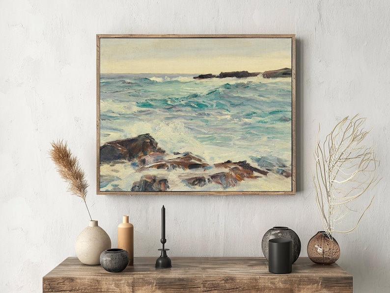 Framed seascape painting on a textured wall shows turbulent waves crashing over rocks. Decor elements include vases, candles, and dried plants nearby.