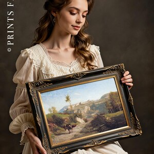 A woman in a white lace dress holds an ornate-framed landscape painting featuring mountains and a winding path. She gazes at it with a serene expression.