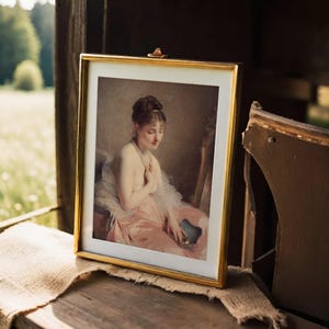 Framed painting of a seated woman in a pink dress, holding a fan, set on a wooden table with a cloth cover, against a soft-focus outdoor background.