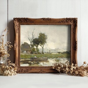 A rustic painting in an ornate wooden frame on a light wooden wall. The scene depicts a tranquil landscape with trees, a cottage, and a river. Dried flowers in jars flank the frame, enhancing the serene, vintage atmosphere.
