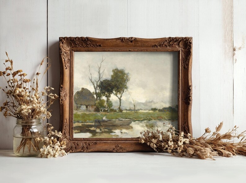 A rustic painting in an ornate wooden frame on a light wooden wall. The scene depicts a tranquil landscape with trees, a cottage, and a river. Dried flowers in jars flank the frame, enhancing the serene, vintage atmosphere.