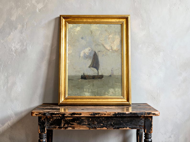 A framed painting of a sailing boat on a calm sea with cloudy skies is placed on a rustic wooden table against a textured gray wall, evoking serenity.