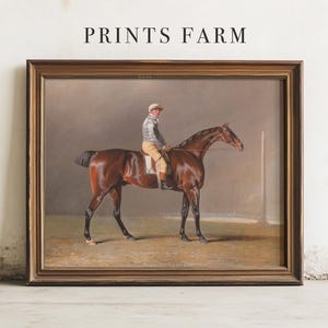 Painting of a jockey on a brown horse, in a wooden frame, leaning against a white wall. The text above reads "Prints Farm."
