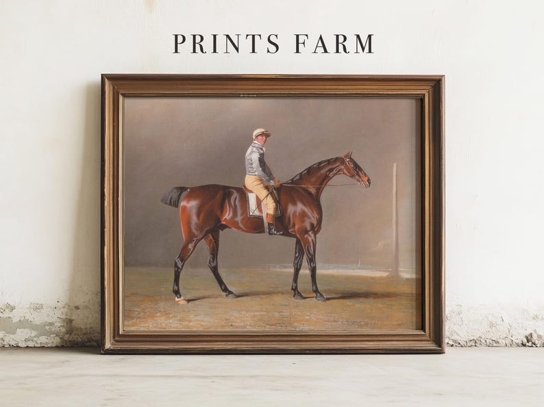 Painting of a jockey on a brown horse, in a wooden frame, leaning against a white wall. The text above reads "Prints Farm."