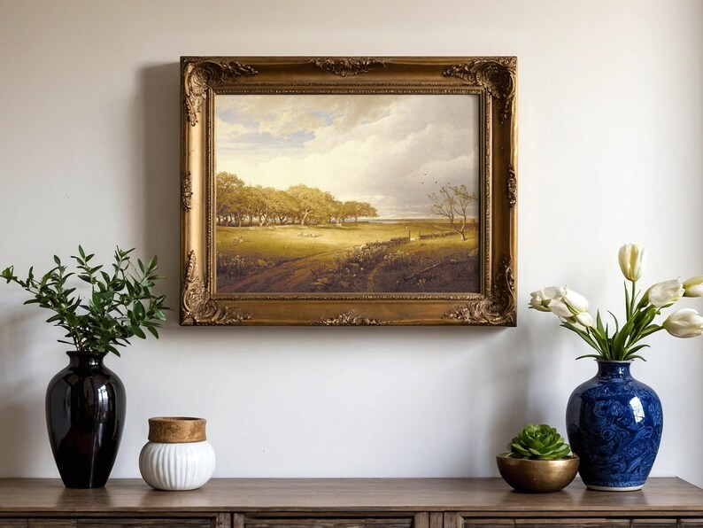 A framed landscape painting is centered on a wall, depicting a serene countryside scene. Below, a wooden console holds vases with flowers and greenery.