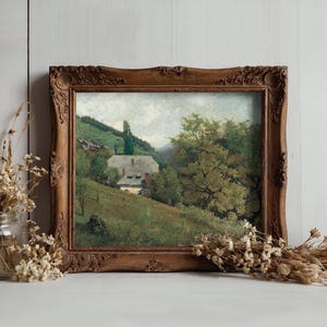 A vintage painting in an ornate wooden frame depicts a serene countryside with a house, trees, and hills. Nearby, dried flowers in a glass jar enhance the rustic ambiance.