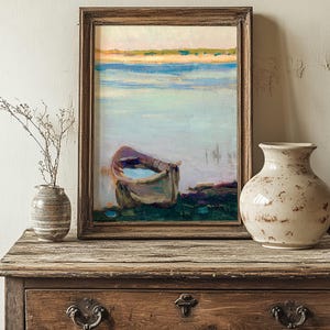 Framed painting of a boat on a calm sea with soft, pastel colors, resting on a rustic wooden dresser. A dried plant and ceramic vase add vintage charm.