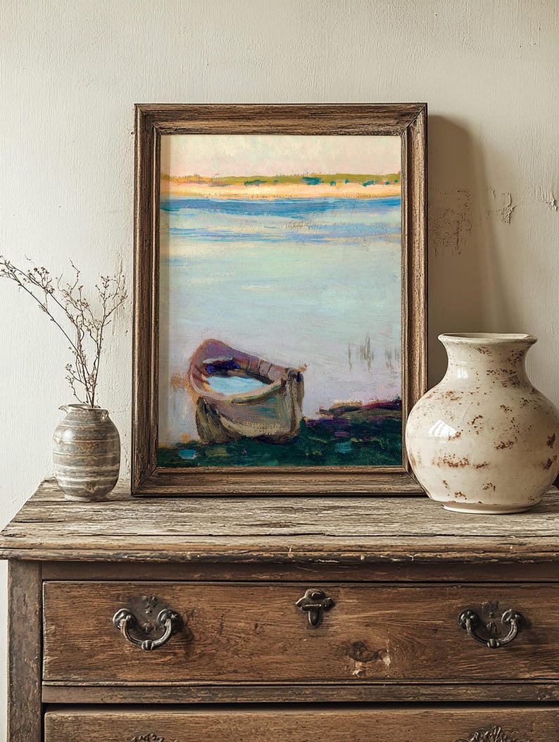 Framed painting of a boat on a calm sea with soft, pastel colors, resting on a rustic wooden dresser. A dried plant and ceramic vase add vintage charm.