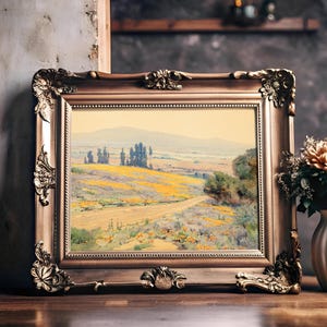 A framed landscape painting on a wooden shelf features a serene countryside, with yellow fields and distant trees. Beside it, a vase with peach roses adds warmth.