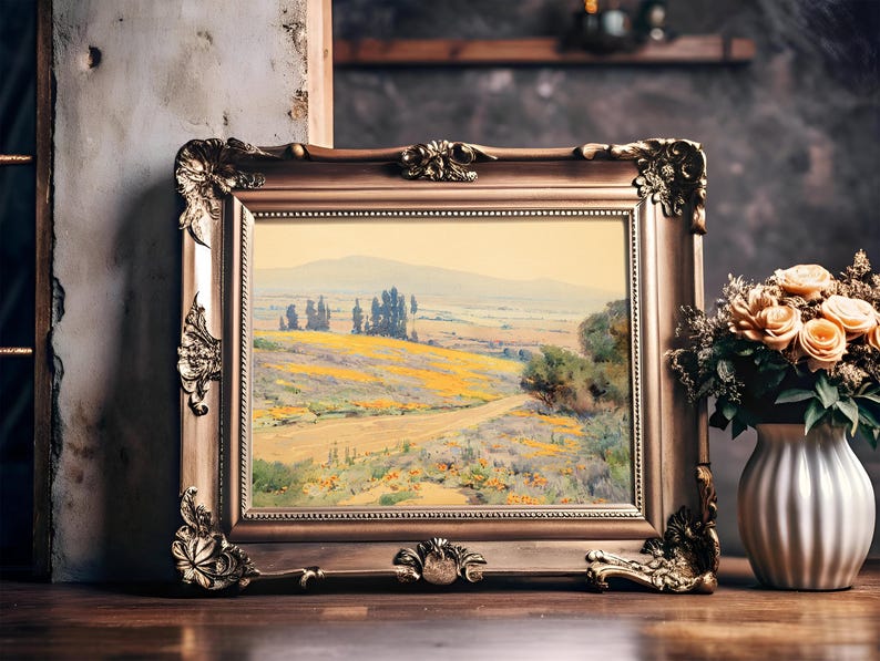 A framed landscape painting on a wooden shelf features a serene countryside, with yellow fields and distant trees. Beside it, a vase with peach roses adds warmth.