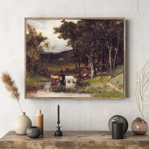 A framed painting of cows by a pond in a lush, forested landscape hangs above a rustic table. Vases with dried plants add a natural touch.