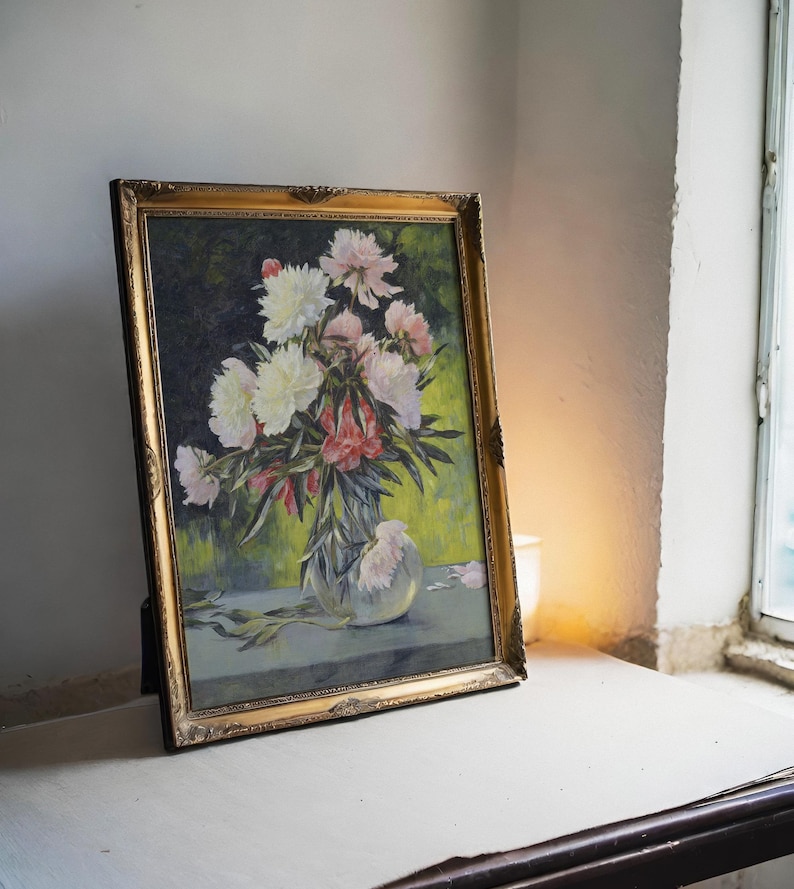 A framed painting of vibrant peonies in a vase, set on a table by a window. Soft light casts a warm glow, highlighting the floral detail and rustic texture.