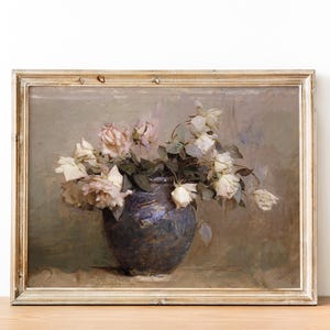 A framed painting of a still life featuring a blue ceramic vase filled with white and pink roses. The roses are wilting and have a vintage aesthetic. The background is a muted brown.