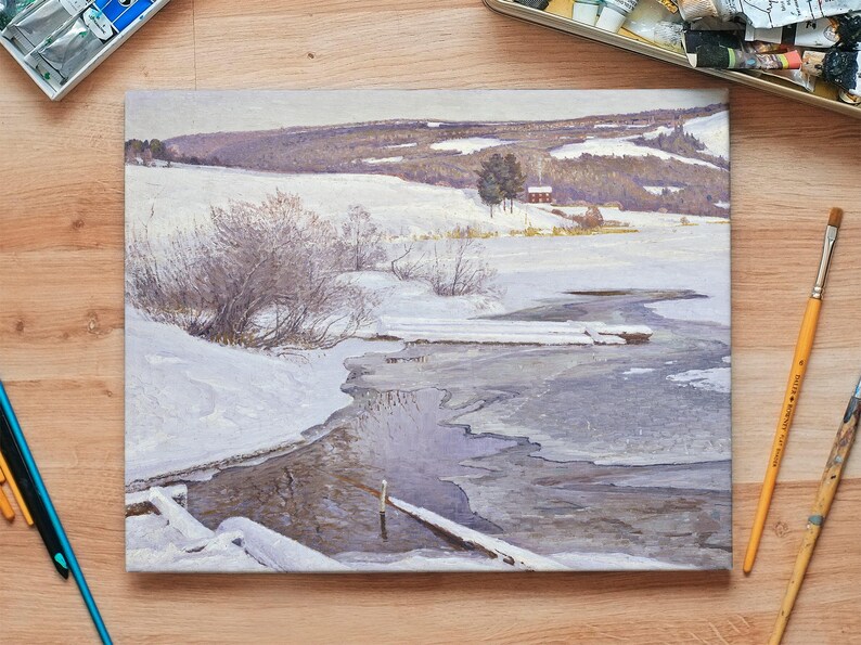 A serene winter landscape painting on a table with art supplies. Snow-covered hills, bare trees, and a frozen river create a peaceful, contemplative tone.
