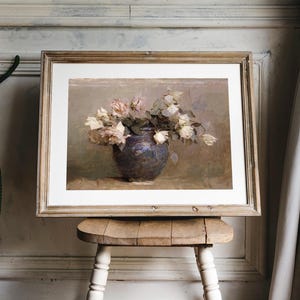 A framed painting of a bouquet of white roses in a dark blue vase. The roses are arranged in a loose, natural style, and the vase is sitting on a table with a light brown tablecloth.