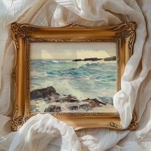 A painting of a turbulent sea with waves crashing against rocks, set in a detailed, ornate gold frame. The frame rests on crumpled, soft white fabric.
