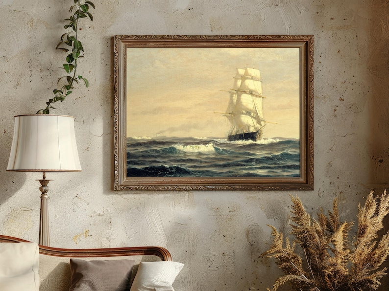 A framed painting of a tall sailing ship navigating rough seas, hung on a textured beige wall. To the left, a white lampshade on a tall lamp and a green vine with small leaves trails from the top left corner. Below the painting, part of a bed with a wooden headboard and pillows in neutral colors is visible. To the bottom right, a bunch of dried, golden-brown pampas grass is arranged in a vase.