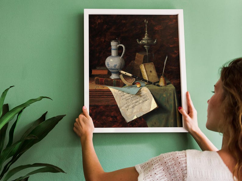 A framed painting of a still life with a blue and white ceramic pitcher, a silver oil lamp, a quill pen, and a sheet of music on a wooden table.