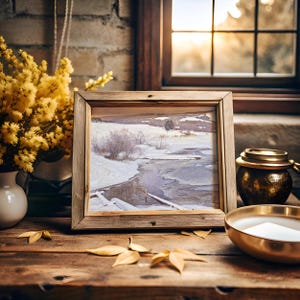A framed winter landscape photo sits on a wooden table, surrounded by yellow flowers and golden decor. Warm light filters through a window, creating an inviting atmosphere.
