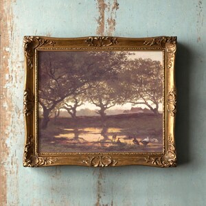 A framed painting on a vintage wall shows a serene landscape with trees and birds by a pond at sunset, conveying a peaceful and nostalgic mood.