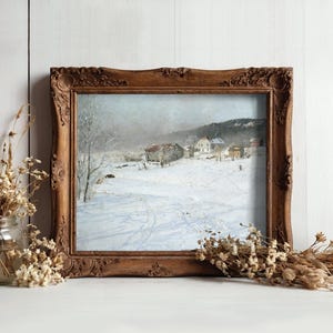 A rustic wooden frame encases a winter landscape painting, featuring snow-covered fields and distant houses. Dried flowers flank the frame, creating a cozy atmosphere.