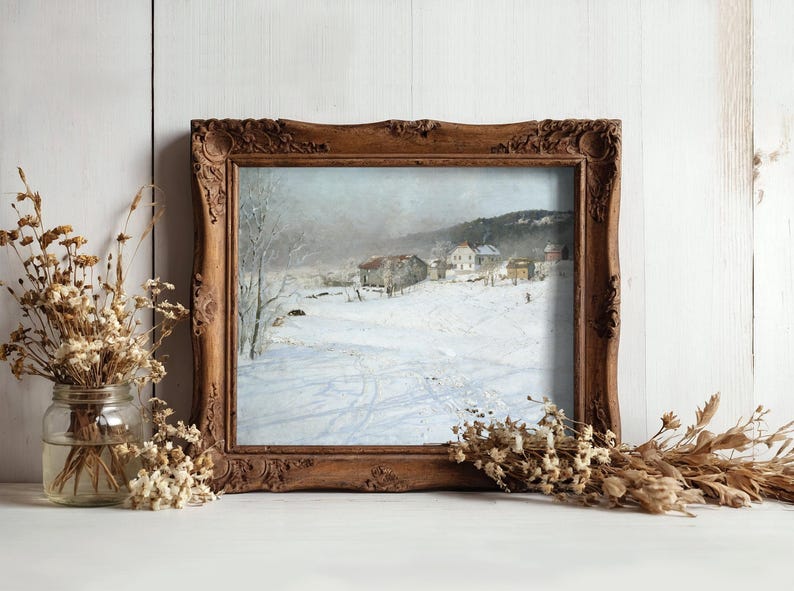 A rustic wooden frame encases a winter landscape painting, featuring snow-covered fields and distant houses. Dried flowers flank the frame, creating a cozy atmosphere.