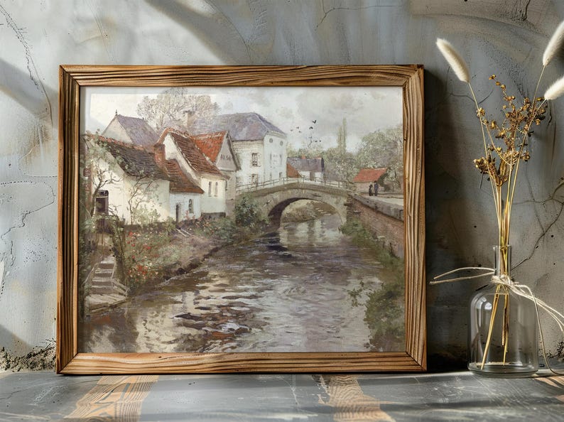 Painting of a serene village scene with a stone bridge over a river, surrounded by rustic houses and trees. Framed in wood, evoking a peaceful, nostalgic mood.