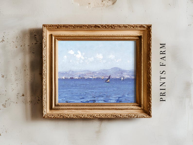 A framed seascape painting depicts a sailboat on a blue ocean with distant hills under a cloudy sky. The frame is ornate and gold, hung on a textured wall.