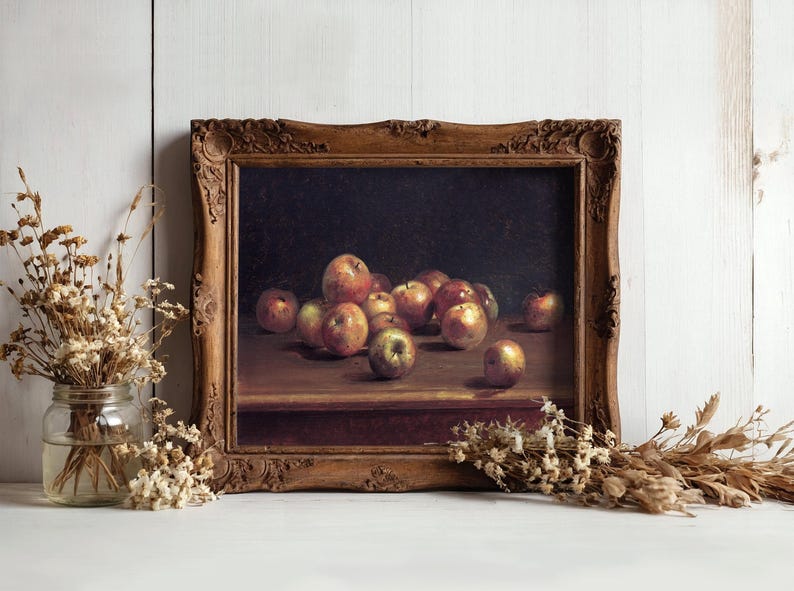 A framed still-life painting of apples on a table, set against a white wooden wall. Dried flowers in vases flank the artwork, adding rustic charm.
