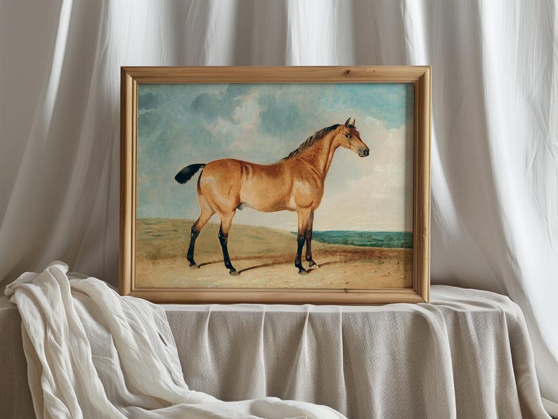Framed painting of a majestic brown horse standing on a plain with a cloudy sky backdrop, set against soft white fabric, exudes elegance and calm.
