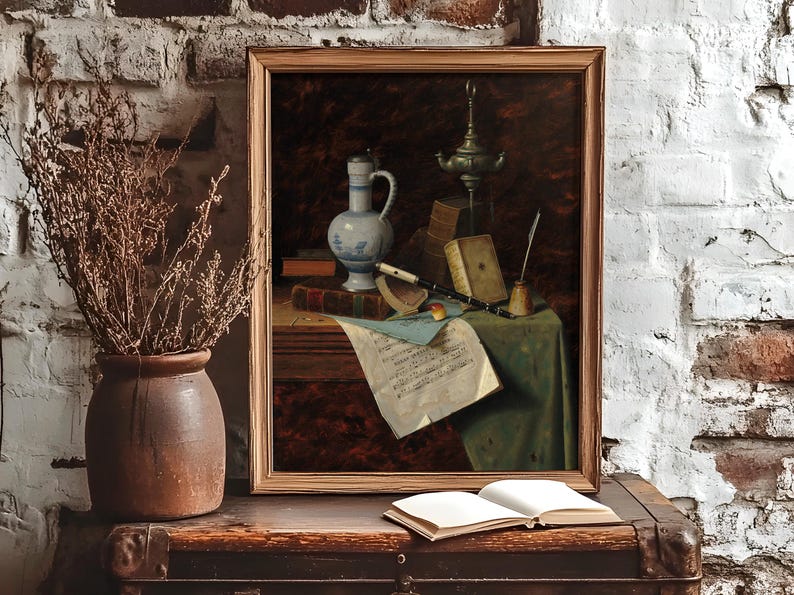 A framed still life painting on a rustic table against a white brick wall. The table holds a ceramic vase with dried branches and an open book. The painting features various objects, including a jug, books, a candle, and sheet music, conveying a vintage, scholarly atmosphere.