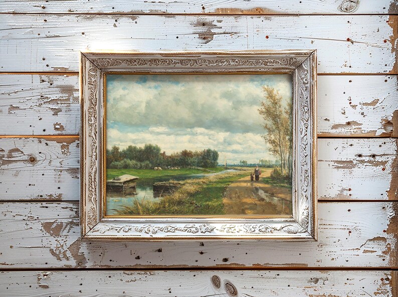A framed landscape painting on a rustic wooden wall. The scene depicts a serene countryside path near a river under a cloudy sky, conveying tranquility.