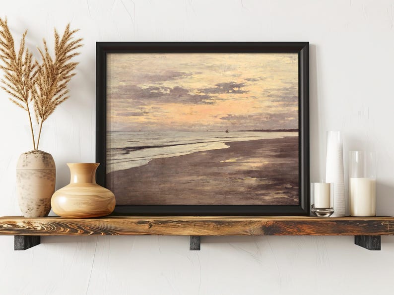 A framed painting of a serene beach at sunset, with gentle waves and pastel skies, displayed on a wooden shelf with vases and candles, evoking tranquility.
