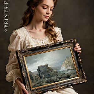 A woman in a vintage white dress holds a framed seascape painting. The scene depicts rocky cliffs and waves. The atmosphere is calm and elegant.