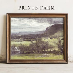 Framed landscape painting with cloudy sky and mountains, set against a plain wall. The scene conveys a calm, pastoral feel. Text above reads "Prints Farm."