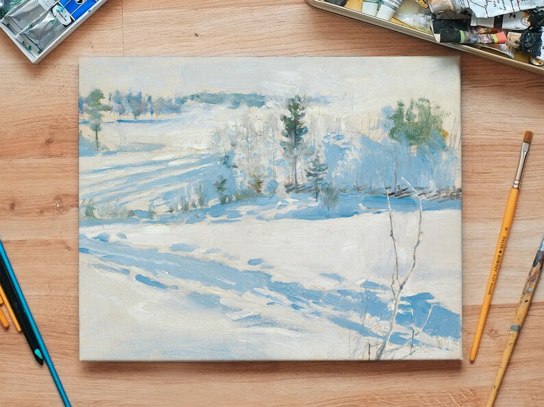 A winter landscape painting sits on a wooden table surrounded by paintbrushes and art supplies. The scene depicts snowy fields with trees, creating a serene and calm atmosphere.