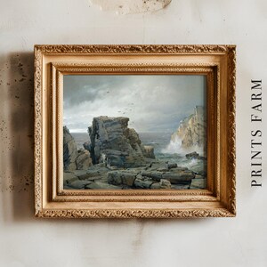 Framed seascape painting with rugged rocks and crashing waves, set against a cloudy sky. Mounted on a textured wall with “PRINTS FARM” text beside it.