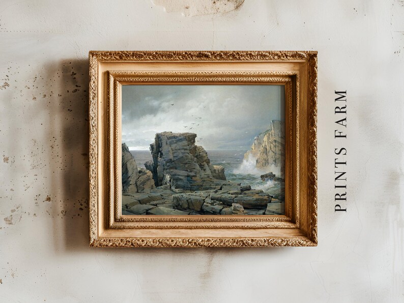Framed seascape painting with rugged rocks and crashing waves, set against a cloudy sky. Mounted on a textured wall with “PRINTS FARM” text beside it.