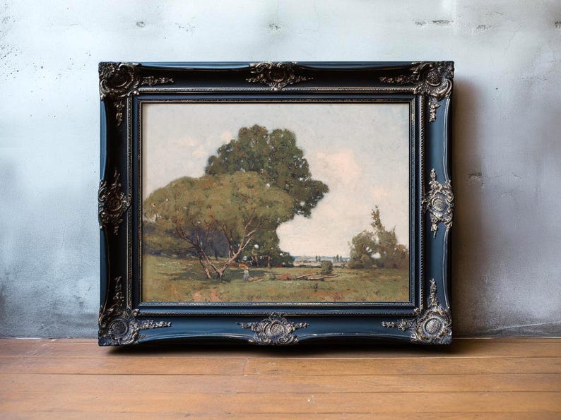 A landscape painting of a park scene with large, leafy trees and a person sitting on the grass, framed in an ornate black and silver frame, leaning against a textured, light-colored wall on a wooden floor.