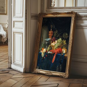 The image shows a classical still life painting displayed on an ornate, gold-colored frame, leaning against an elegant, detailed wall in a room with wooden parquet flooring. The painting depicts a detailed arrangement of fruits, a lobster, and decorative objects on a dark, rich fabric background, emphasizing the opulence and craftsmanship of the artwork.