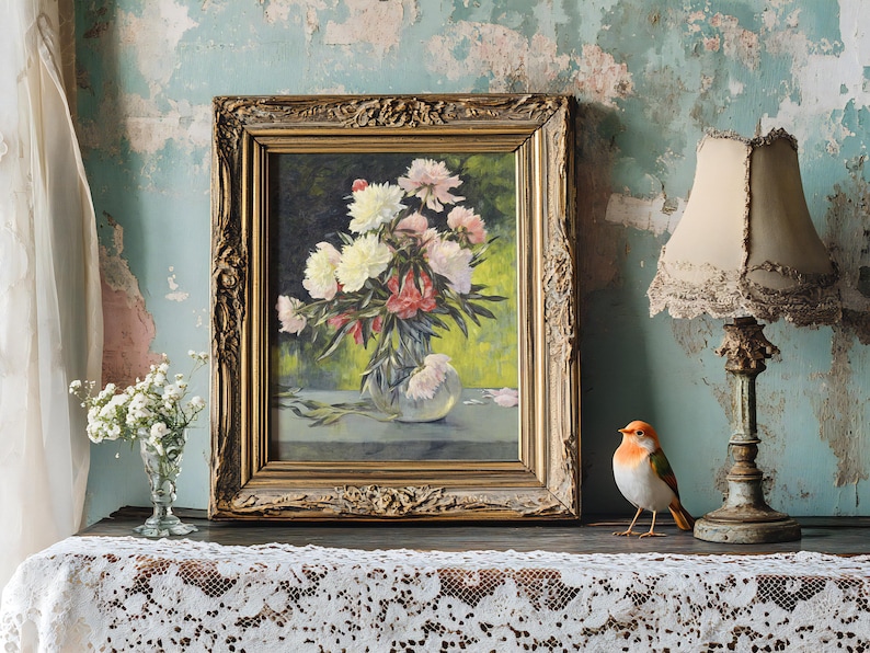 Framed floral painting on an antique table with lace cloth, beside a vintage lamp and bird figurine. The setting is rustic and charming.