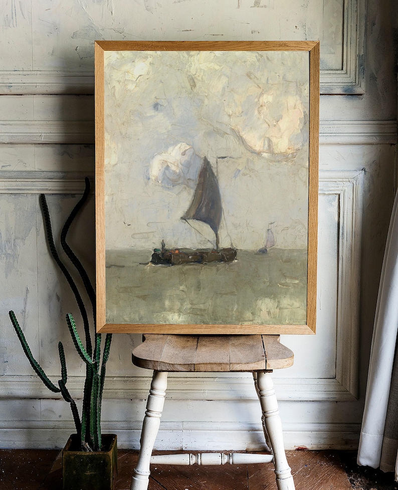 A framed painting of a sailboat on a calm sea with a cloudy sky. The painting is in a light wood frame and is hanging on a white wall.