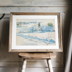 Framed landscape painting of a snowy field and distant trees on a wooden stool. Soft, natural light filters through beige curtains, evoking calm tranquility.