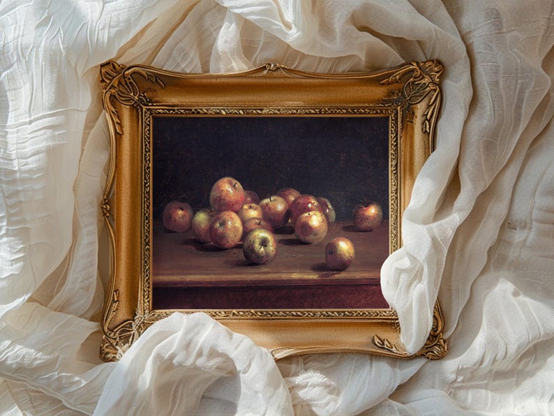 A framed still life painting of apples on a wooden table, surrounded by soft white fabric. The scene conveys a classic and serene tone.
