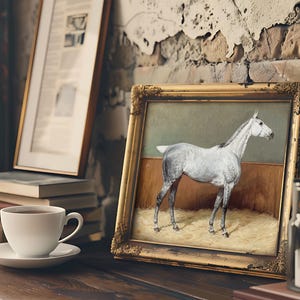 A framed painting of a white horse leans against a rustic, textured wall on a wooden shelf. Nearby, a cup of coffee and stacked books create a cozy atmosphere.