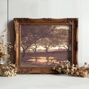 Framed landscape painting of trees at sunset, reflecting in a pond. Rustic wooden frame. Dried flowers in a jar and scattered on white surface.