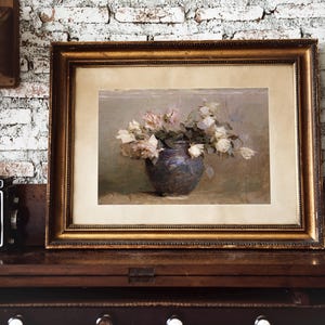 A framed painting of a bouquet of white roses in a blue vase. The roses are arranged in a loose, natural style, and the vase is simple and elegant. The painting is set against a soft, muted background.