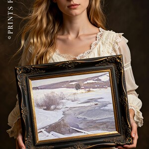 A woman in a vintage white dress holds a framed winter landscape painting depicting a snowy field and icy river, exuding a serene and contemplative mood.